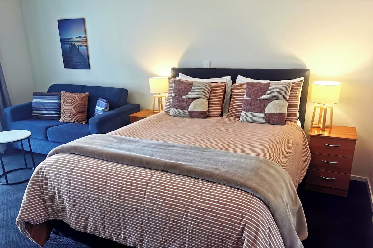 Ein ordentlich eingerichtetes Schlafzimmer mit einem großen Bett, einer Couch, einem kleinen Tisch und zwei Nachttischlampen.