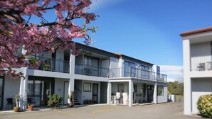 A two-story motel with a balcony on the upper floor, potted plants, and a clear sky.