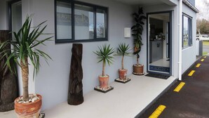 A building with a grey exterior, a covered entrance, and potted plants along the side.