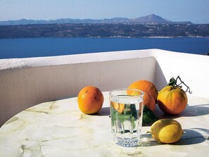 A marble table with a glass of water, oranges, and a lemon on a balcony overlooking a body of water and distant mountains. - Areti Hotel (Chania)