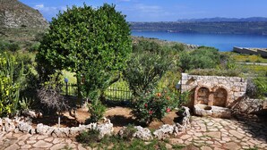 A garden with a stone wall, a tree, and a view of a body of water. - Areti Hotel (Chania)