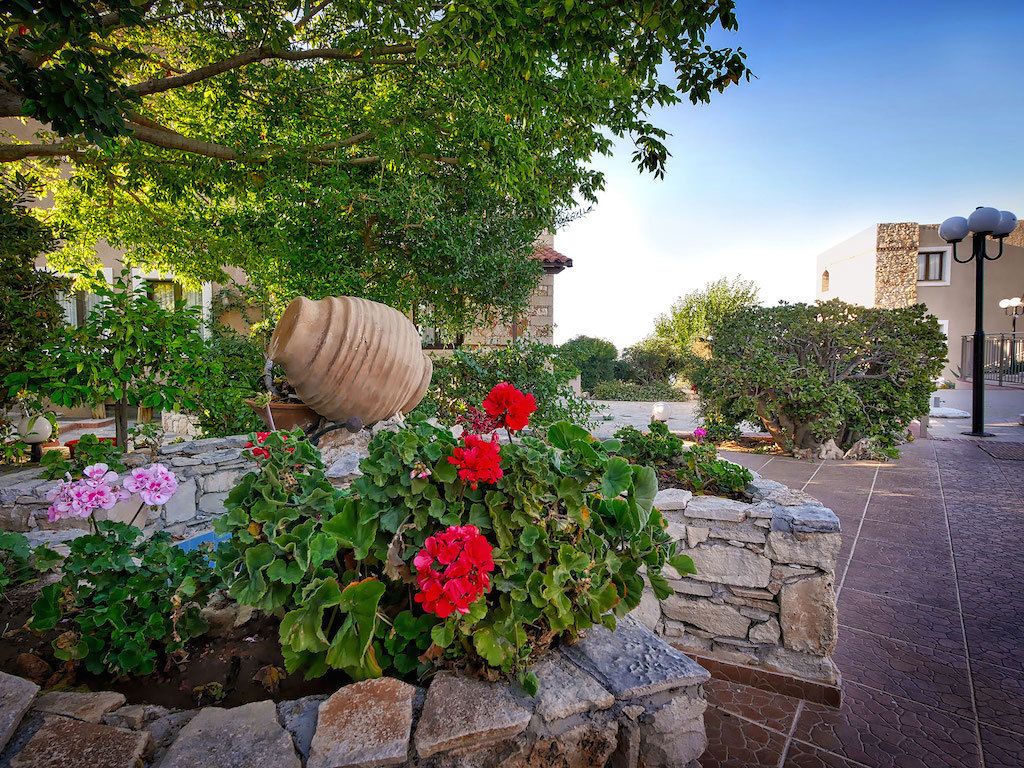 A courtyard with stone walls, red and pink flowers, and a large tree.