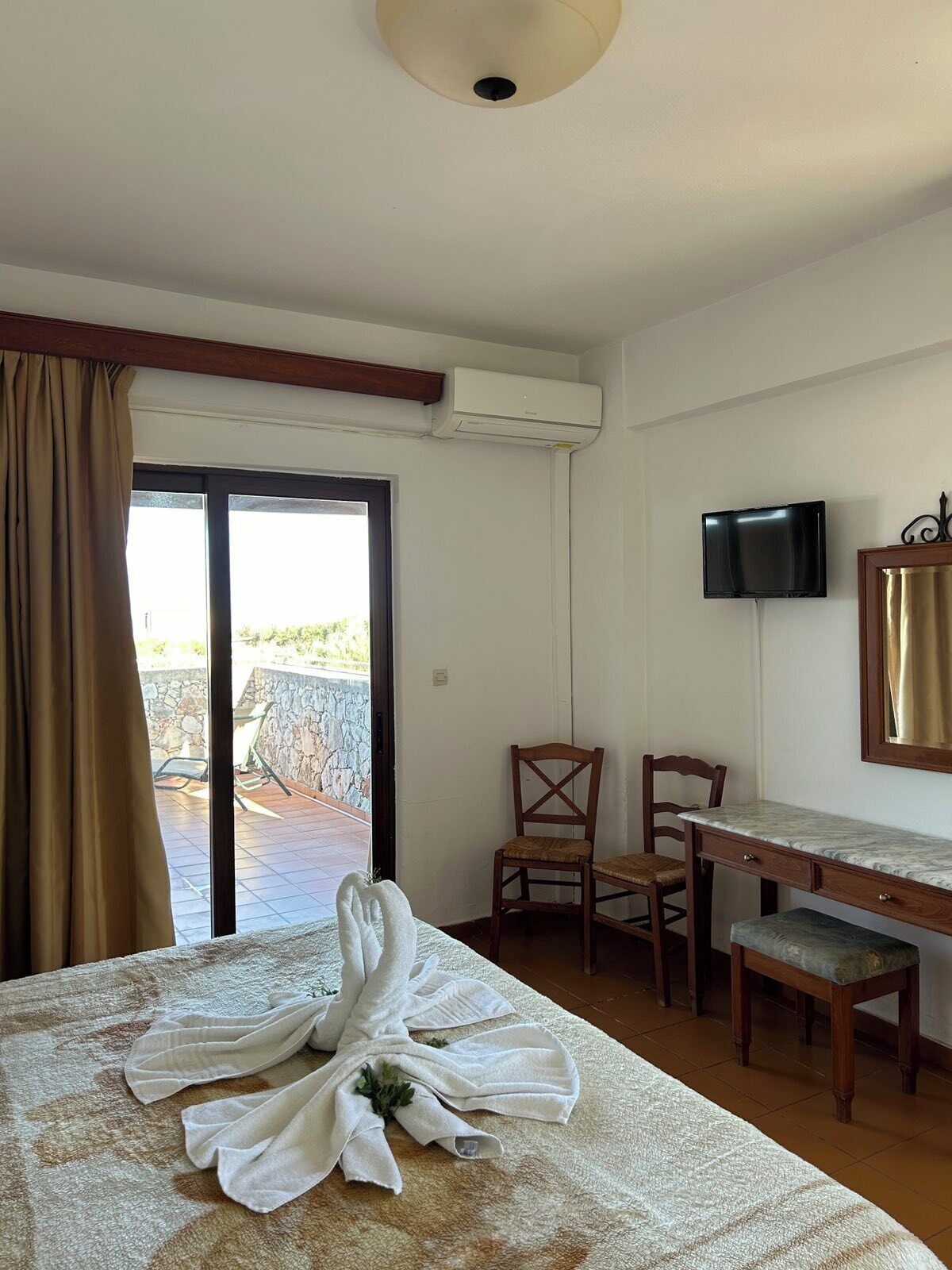 A hotel room with a bed, a desk, a chair, a television, and a sliding glass door leading to an outdoor area.