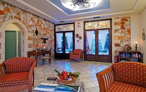 A cozy living room with a stone wall, a fireplace, and a dining area with a table and chairs. - Areti Hotel (Chania)