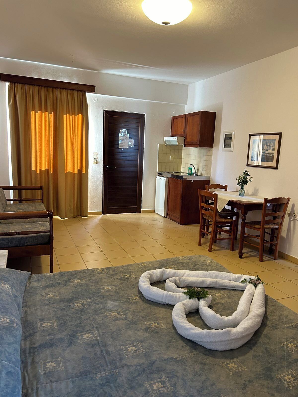Habitación de hotel con cama, escritorio, silla, zona de cocina y mesa de comedor.