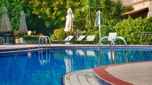 A swimming pool with a tiled deck, lounge chairs, and umbrellas. - Areti Hotel (Chania)