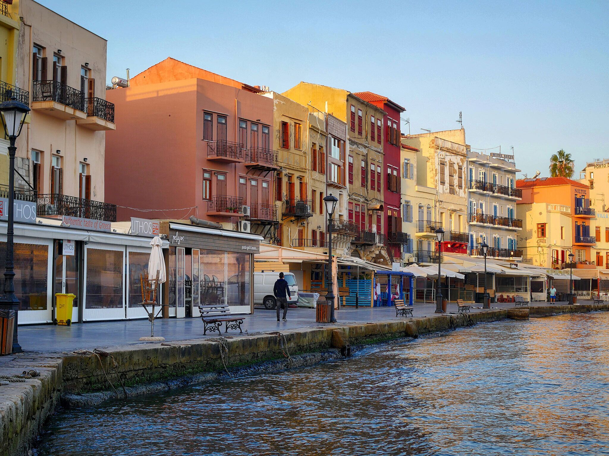A waterfront street with colorful buildings, a café, and a bench by the canal.