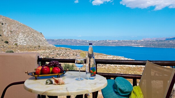 A table with fruits, a glass, and a bottle, overlooking a coastal landscape. - Areti Hotel (Chania)