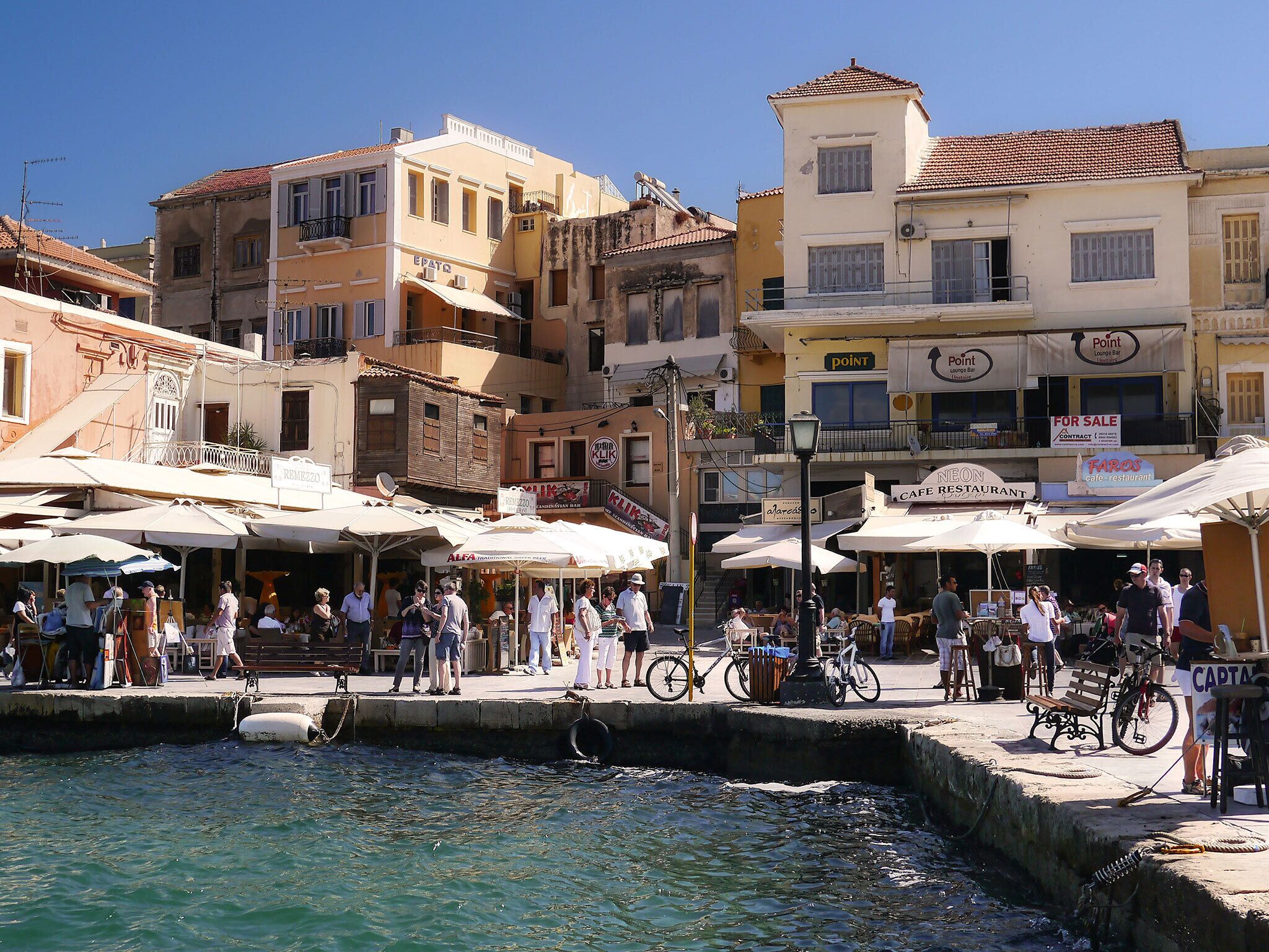 A bustling waterfront area with buildings, outdoor seating, and bicycles.