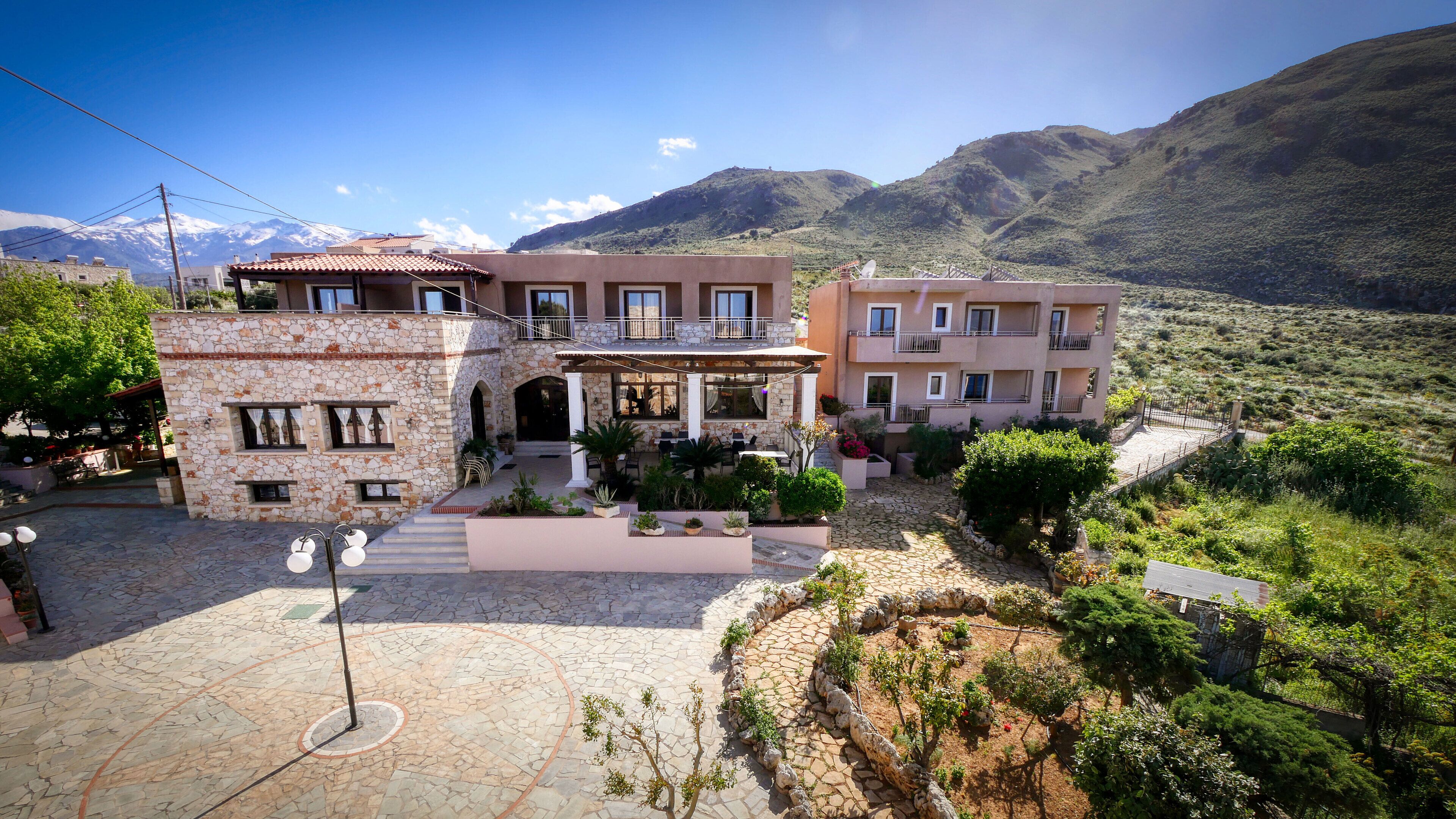 A hotel with a stone facade, outdoor seating, and a mountainous backdrop.