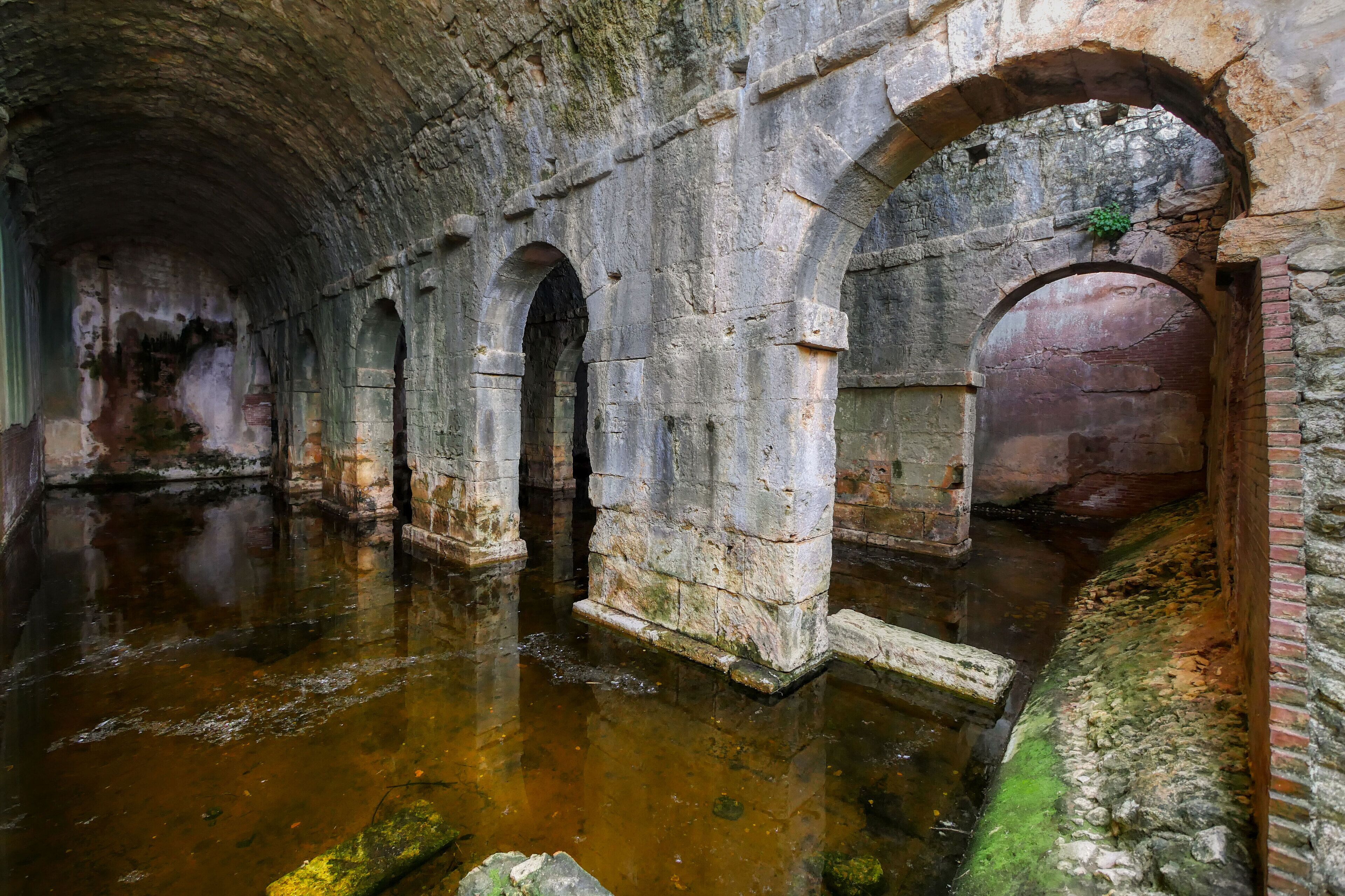 An ancient stone structure with arched passageways and a water-filled floor.