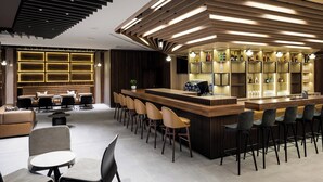 A modern bar area with a wooden bar counter, bar stools, and a seating area with sofas and chairs. - AC Hotel by Marriott Bratislava Old Town (Bratislava)