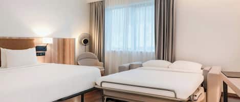 Habitación de hotel con dos camas, una mesita de noche, una lámpara, una lámpara de pie y un ventanal grande con cortinas.