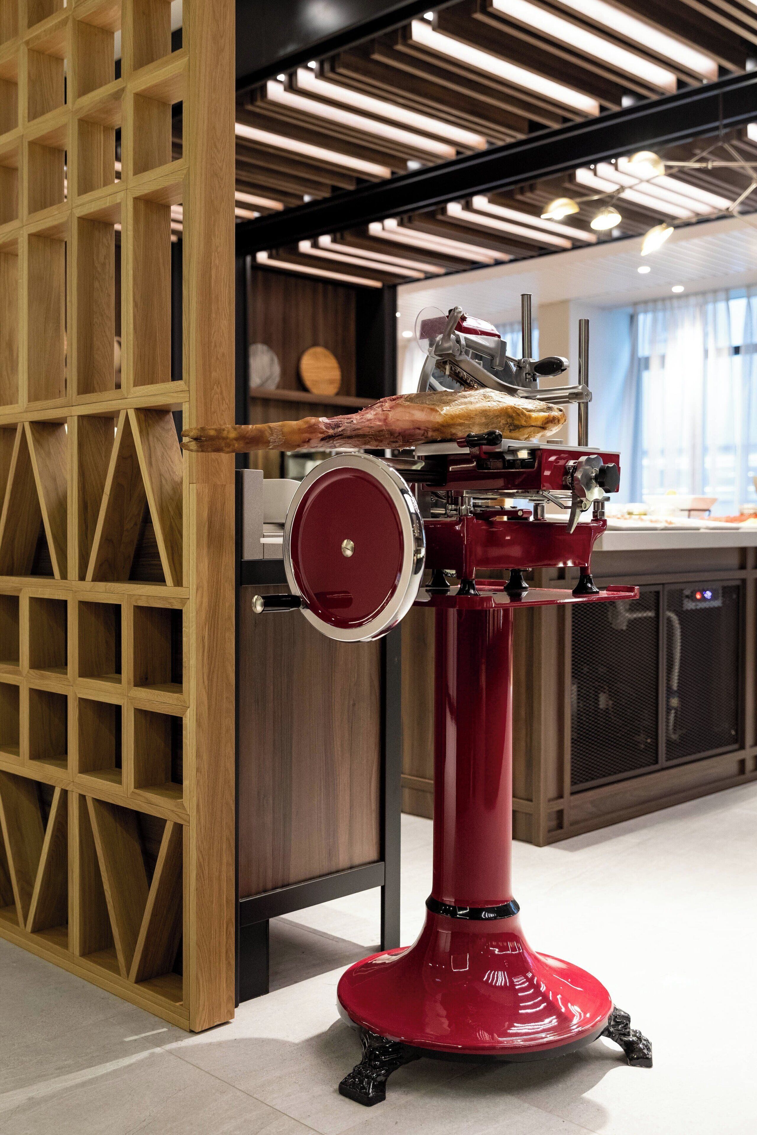 A red espresso machine with a wooden panel and a metal counter in a modern kitchen setting.