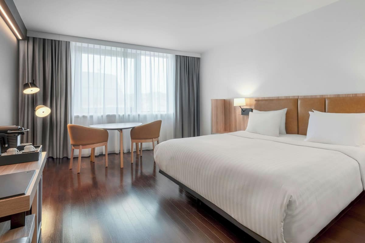 A hotel room with a large bed, a desk with a laptop, a chair, and a window with curtains.