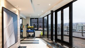 A modern gym with exercise equipment, large windows, and a city view. - AC Hotel by Marriott Bratislava Old Town (Bratislava)