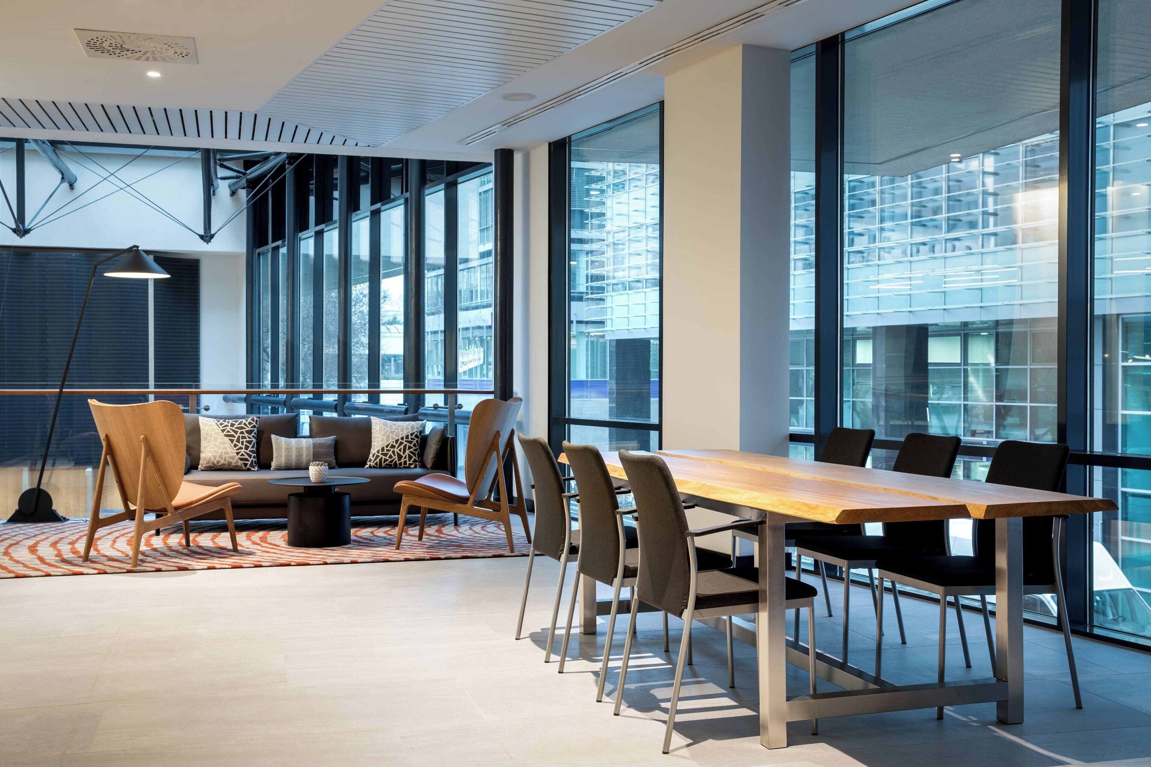 Een moderne vergaderruimte met een lange tafel, stoelen, een bank en grote ramen met uitzicht op de stad.