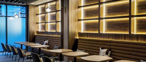 A modern restaurant interior with wooden panel walls, round tables, and cushioned seating.