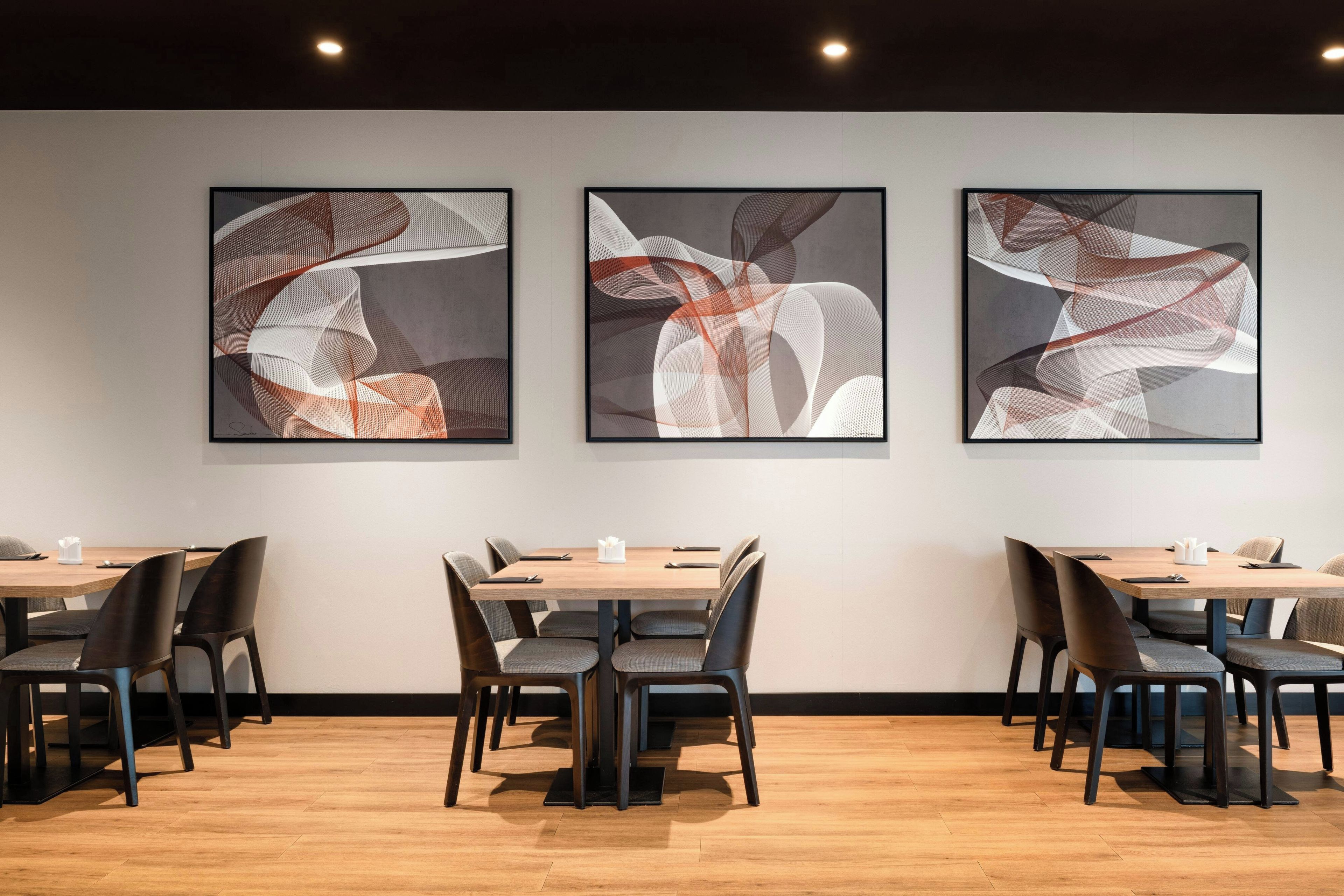 Une salle de conférence moderne, avec trois tableaux abstraits accrochés au mur, des tables en bois et des chaises noires.