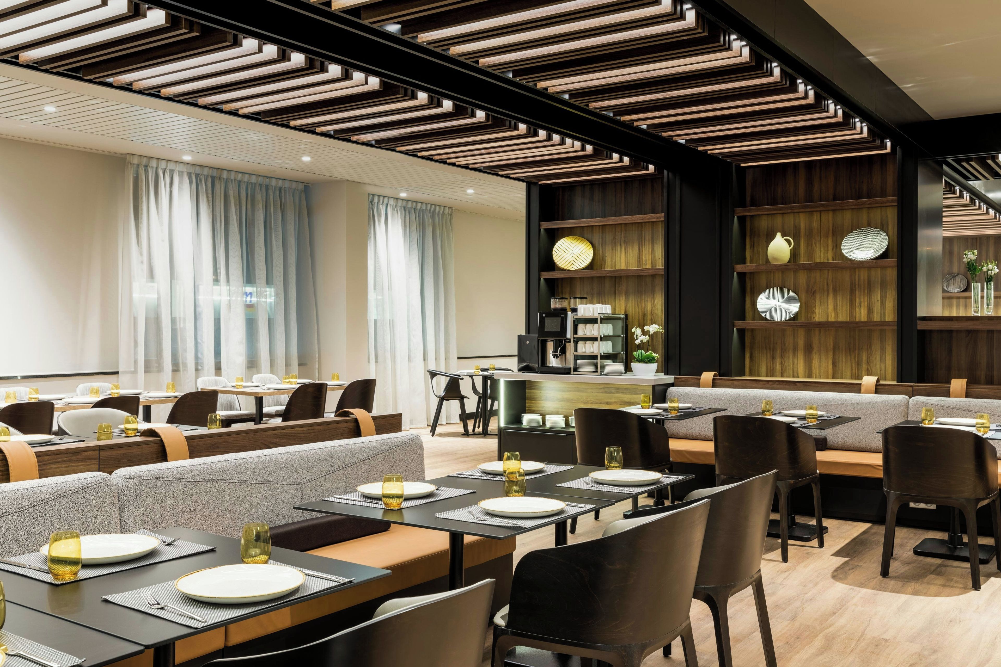 Un restaurante moderno con techos altos, paneles de madera geométricos y una variedad de opciones de asientos, incluyendo cabinas y mesas.
