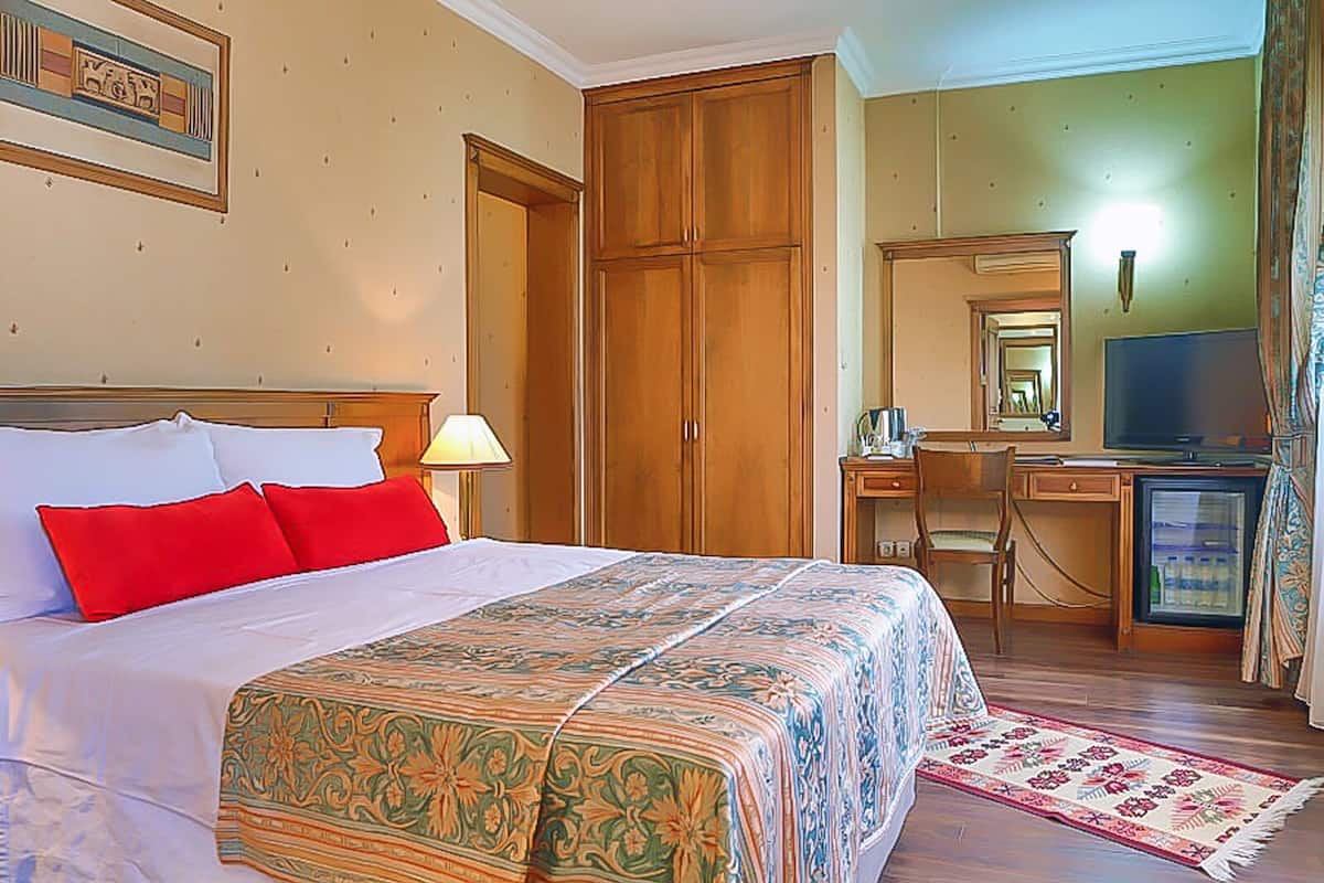 A hotel room with a bed, a desk with a television, a wardrobe, and a mirror.