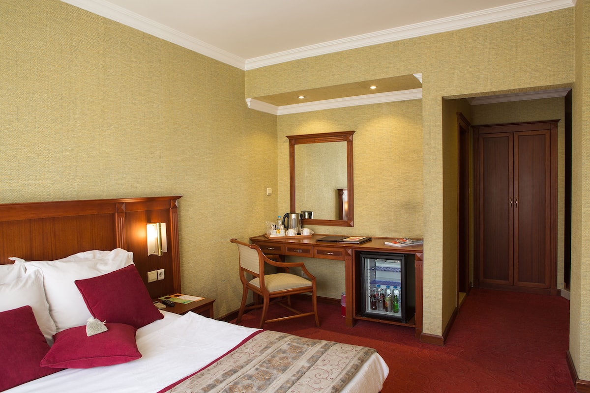 A hotel room with a bed, desk, chair, and a minibar.