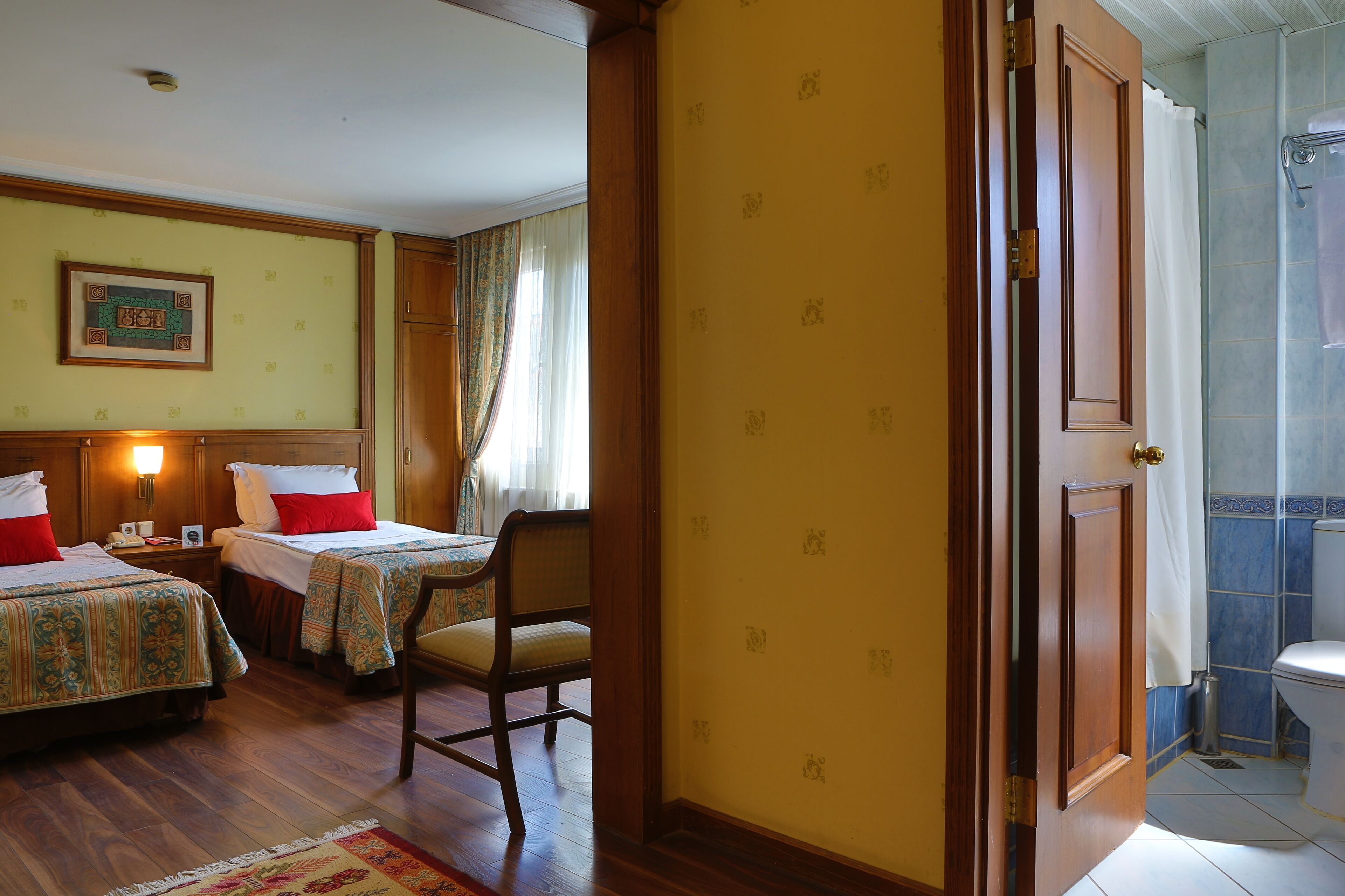 Habitación de hotel con dos camas, una silla de madera, una mesita pequeña y un baño con ducha.