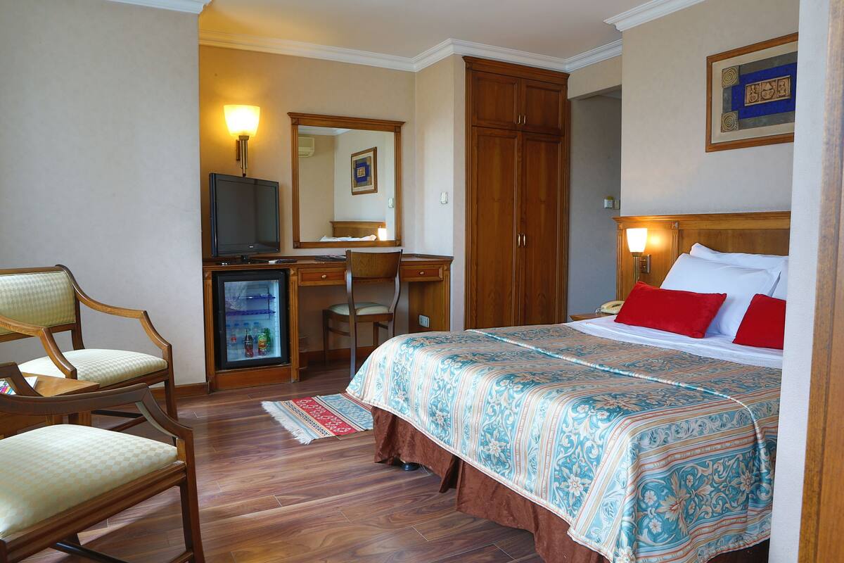 A hotel room with a bed, a desk, a chair, a television, and a wardrobe.