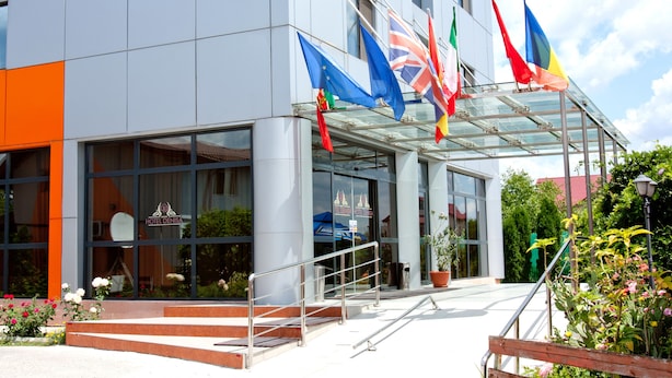 A modern hotel building with a glass entrance and multiple flags. - Denisa Hotel Otopeni (Otopeni)