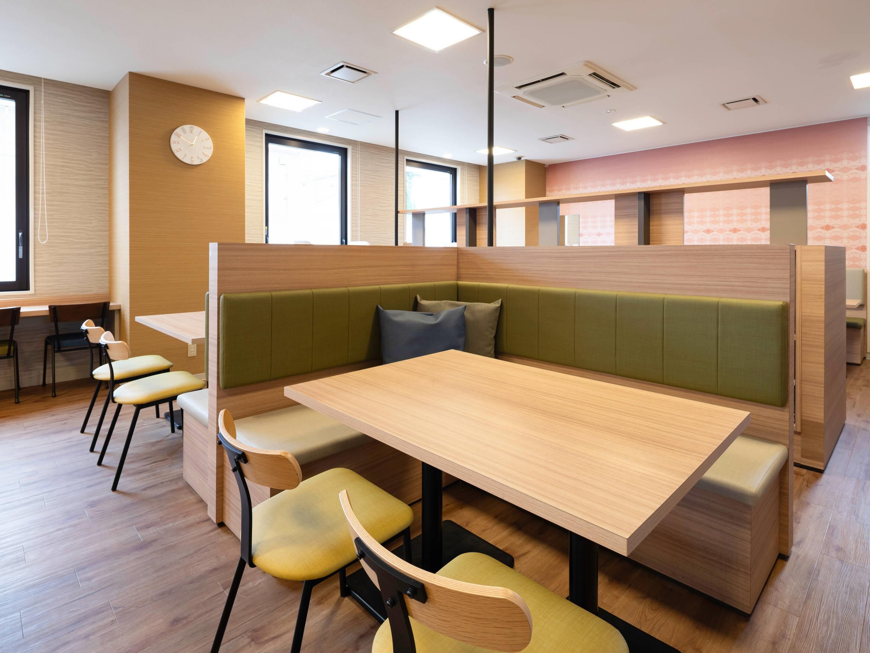 A modern dining area with a wooden table, green cushioned booths, and yellow chairs.