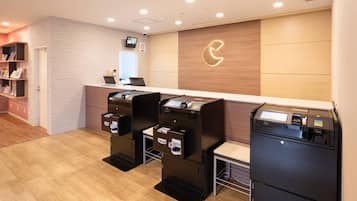 A reception area with a counter, two self-service kiosks, a wall-mounted logo, and a bookshelf with magazines.