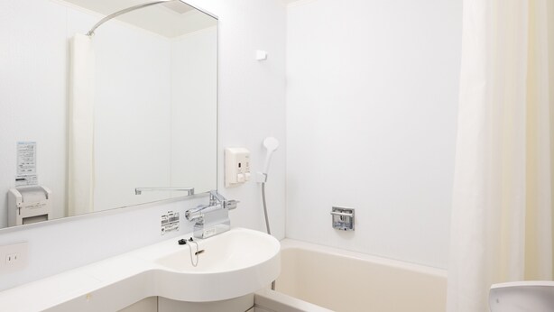 Een moderne badkamer met een witte wastafel, spiegel en badkuip. Er zijn zeepdispensers en een handdoekhouder.