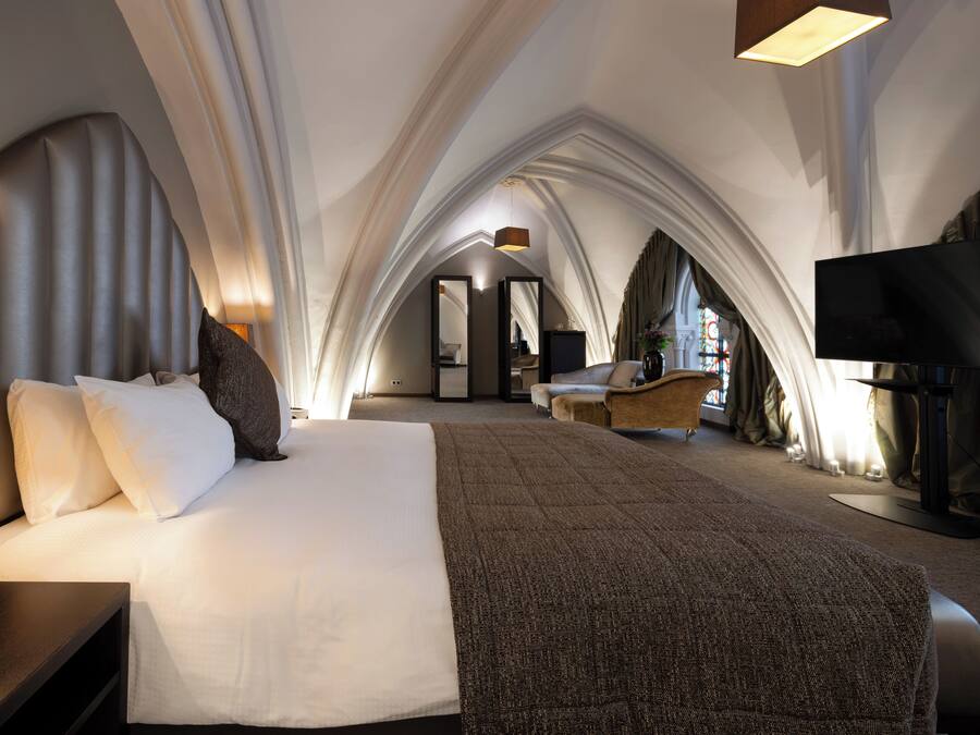 A modern hotel room with a large bed, a nightstand, a TV, and a view of the room's interior.