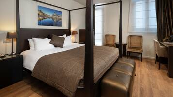 A four-poster bed with a cityscape painting, a desk with two chairs, and a large window with curtains.