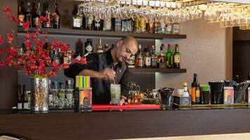 Een bar met flessen drank, een bartender die een drankje bereidt en hangende wijn glazen.