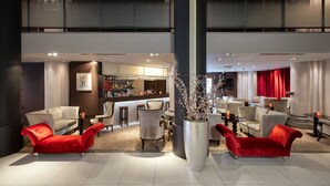 Un moderno vestíbulo de hotel con zona de bar, arreglos de asientos y una gran planta decorativa.