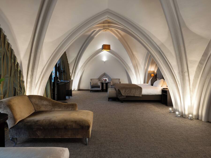 Een kamer met een gewelfde plafond, een bank, een bed en een kleine tafel met een lamp.