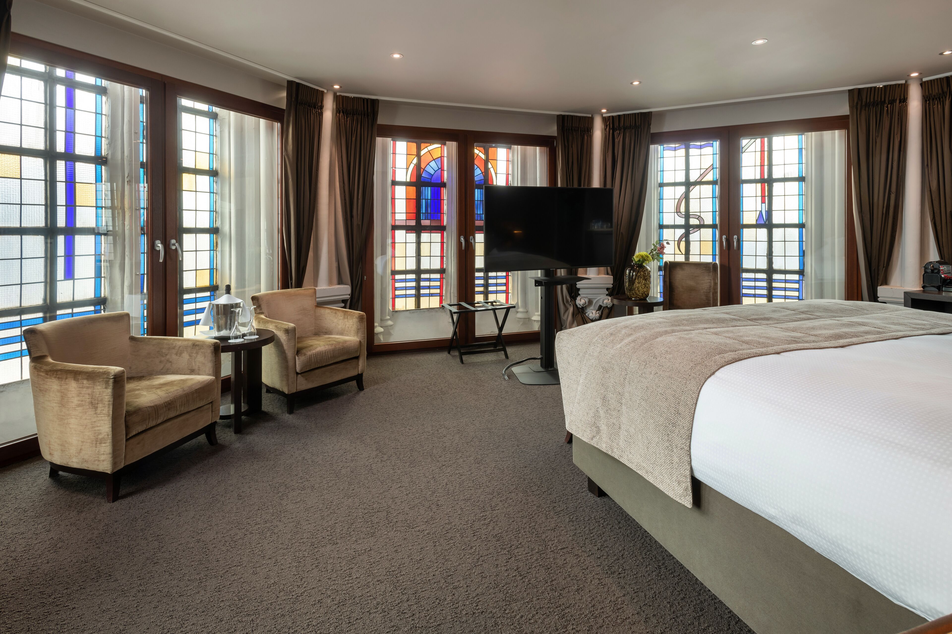 A hotel room with a large bed, two armchairs, a TV, and a small table.