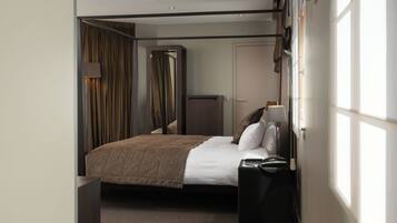 Habitación de hotel con cama, mesita de noche, lámpara, armario y ventana con cortinas.