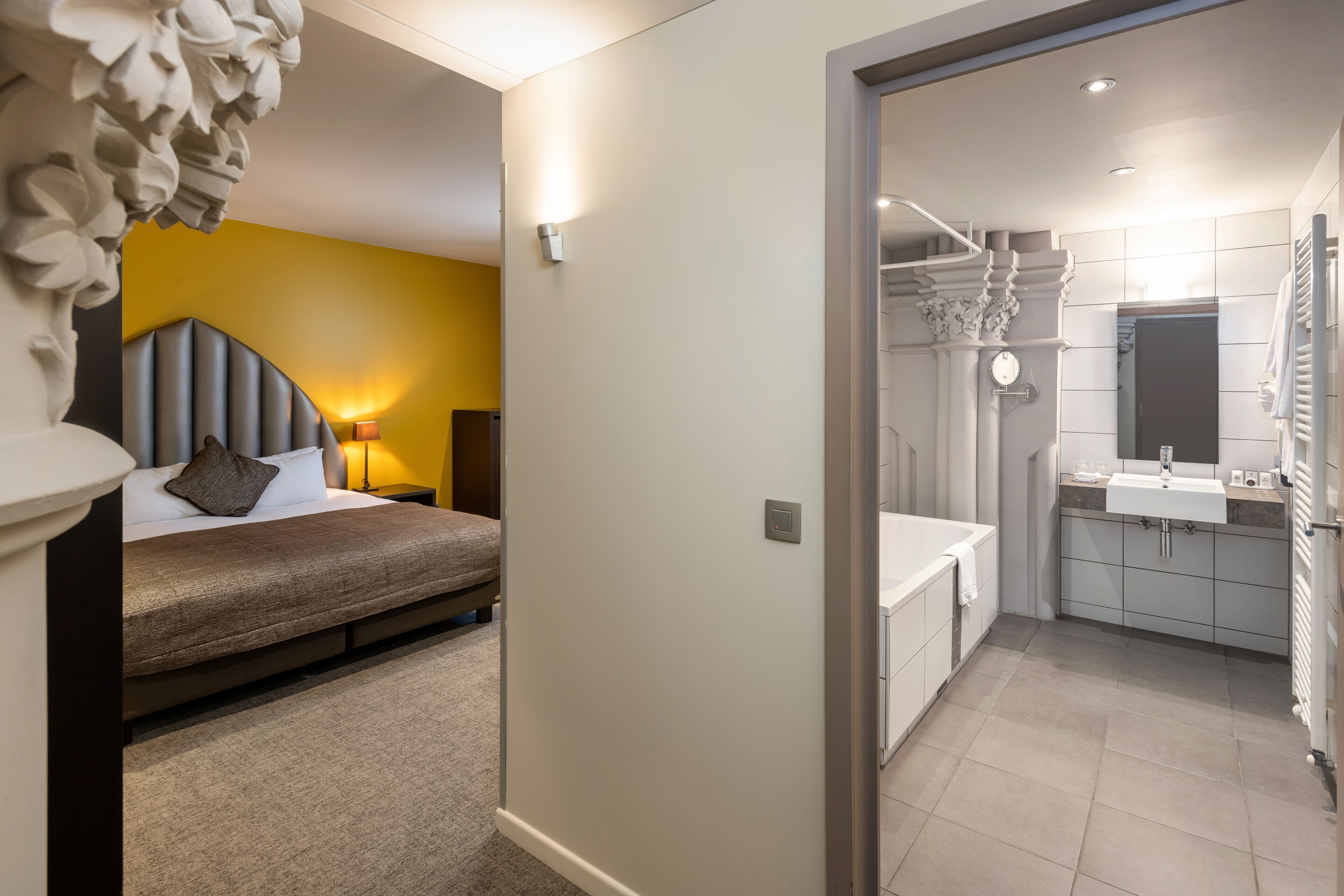 A modern bedroom with a bed, bedside lamp, and a wall-mounted light fixture.