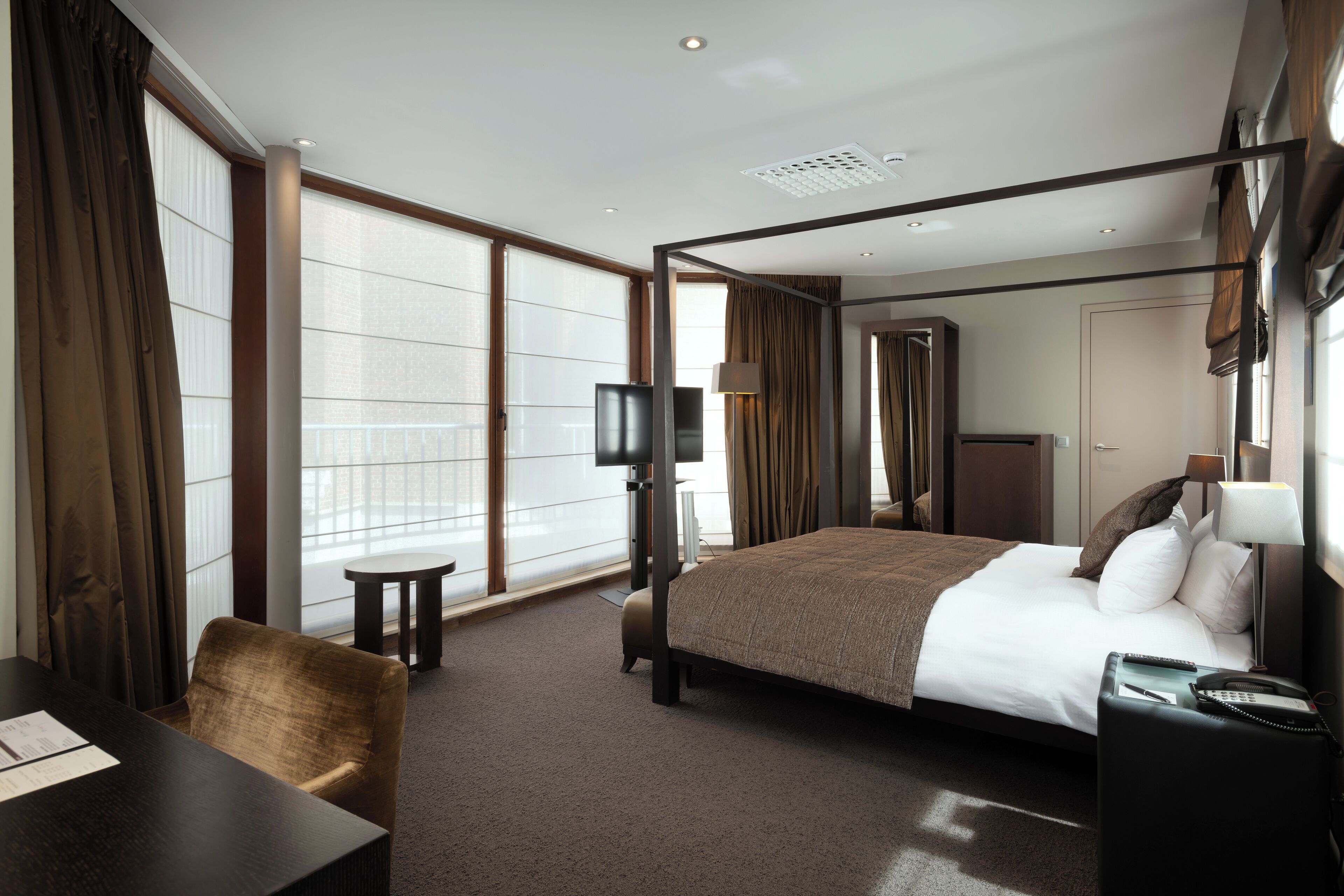 A hotel room with a large bed, a desk, a chair, a TV, and a window with curtains.