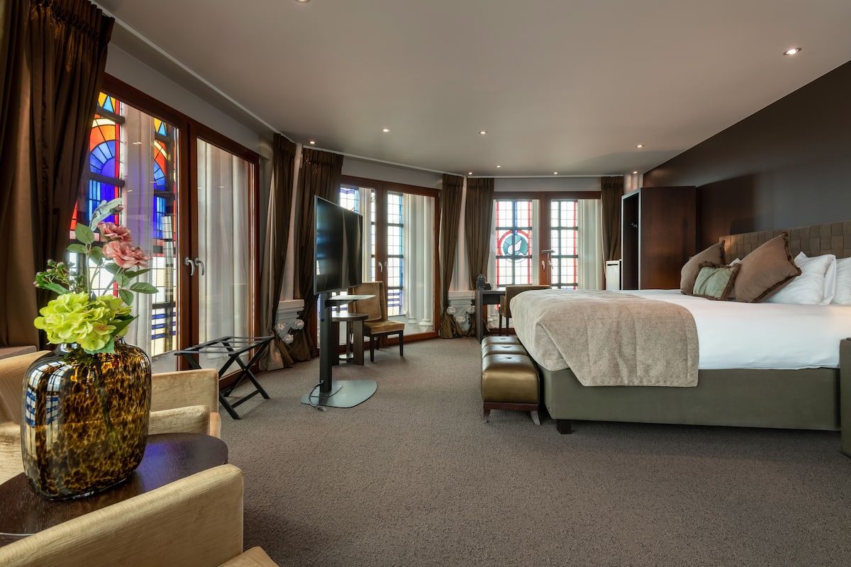 Una habitación de hotel amplia con una cama grande, un escritorio, una silla y un televisor.