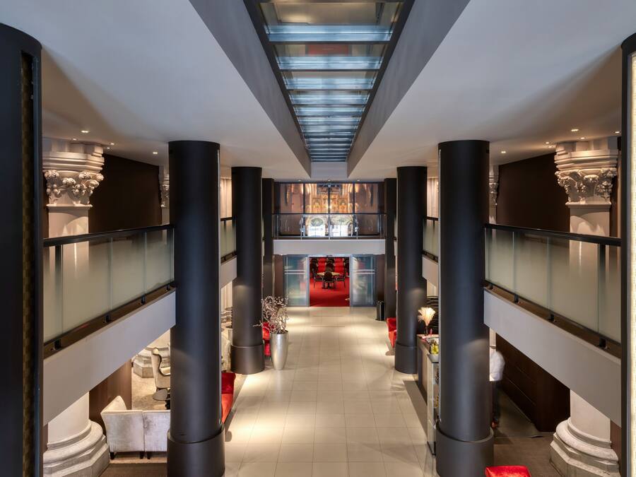 Un hall d’hôtel spacieux, doté d’un espace salon central aux couleurs vives, de grandes colonnes et d’un design moderne au niveau du plafond.