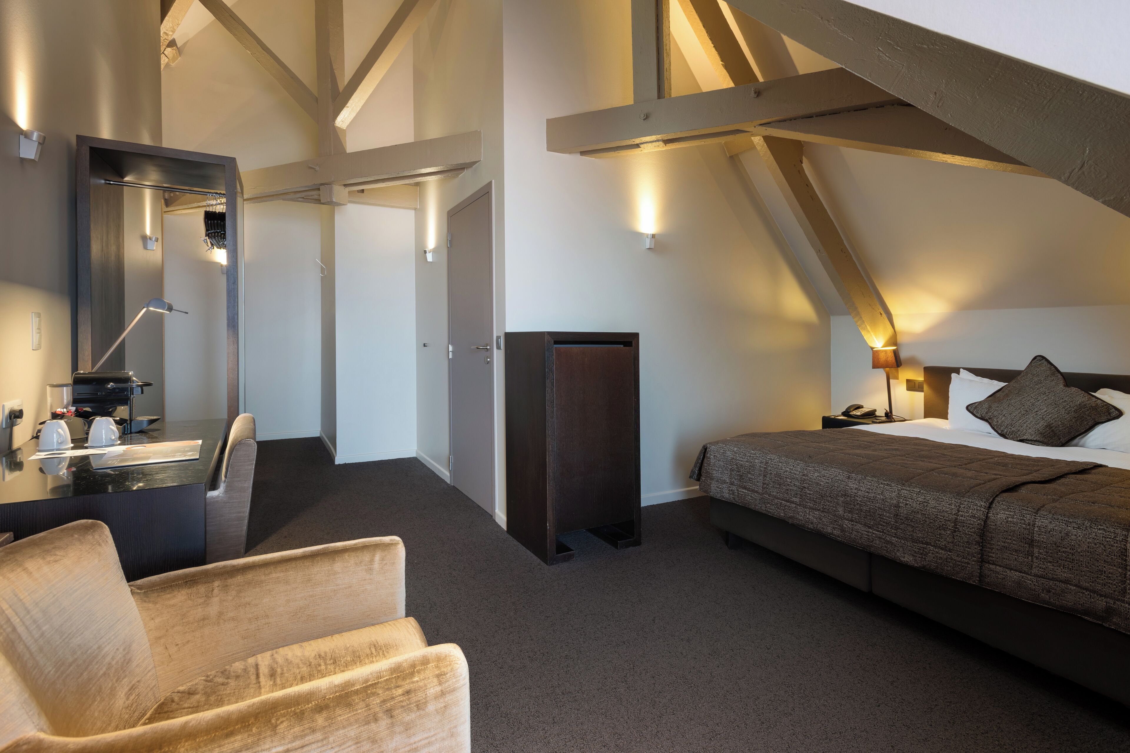 Una habitación de hotel moderna con una cama grande, un escritorio con espejo, una silla y un armario.
