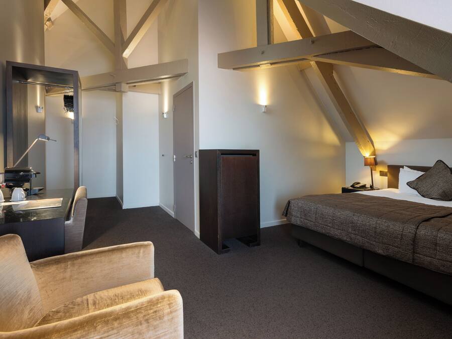 Una habitación de hotel moderna con una cama grande, un escritorio con espejo, una silla y un armario.