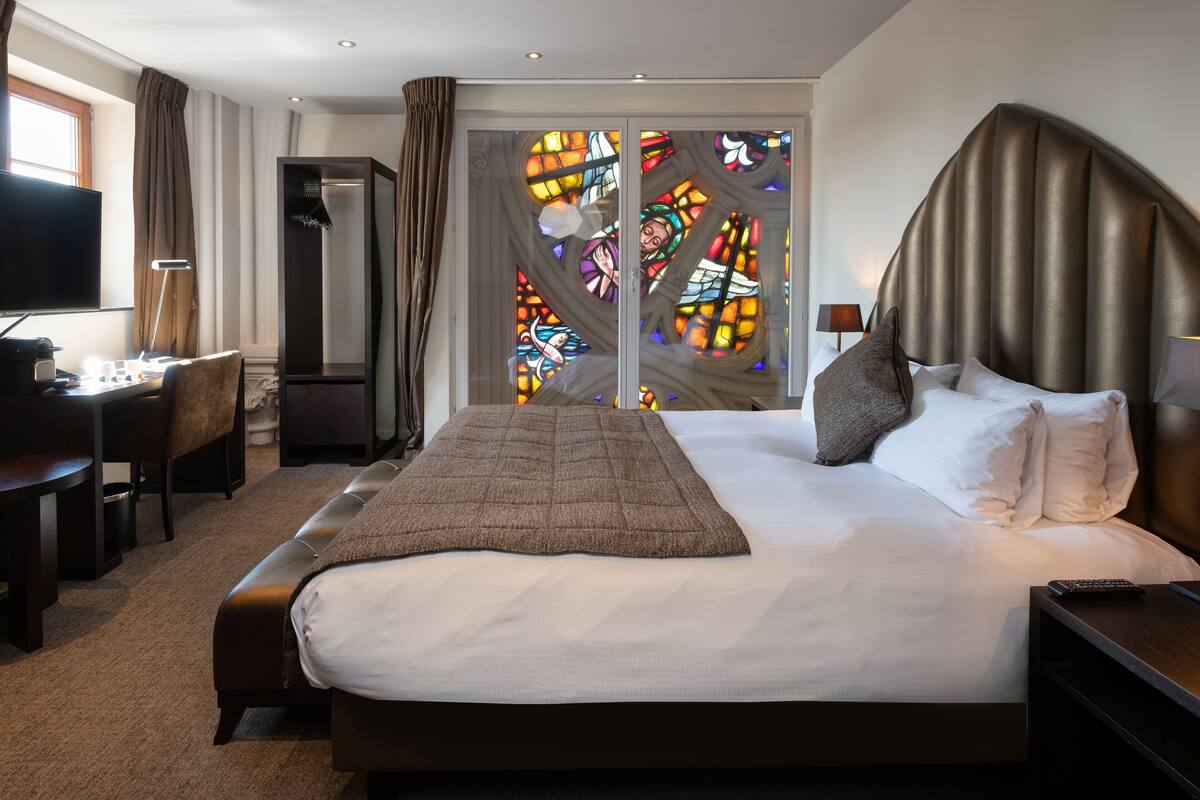 Habitación de hotel con una cama grande, un escritorio con computadora, un televisor y vistas a un vitral.