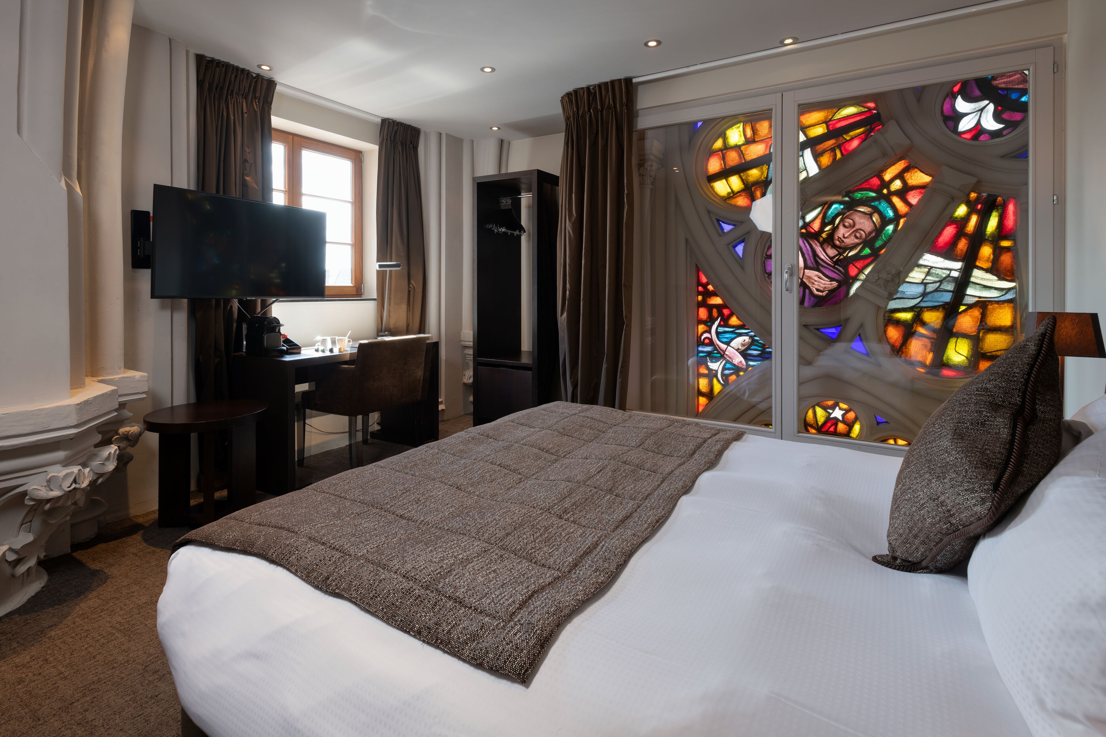 Habitación de hotel con una cama grande, un escritorio, un televisor de pantalla plana, una silla y vistas a vidrieras.