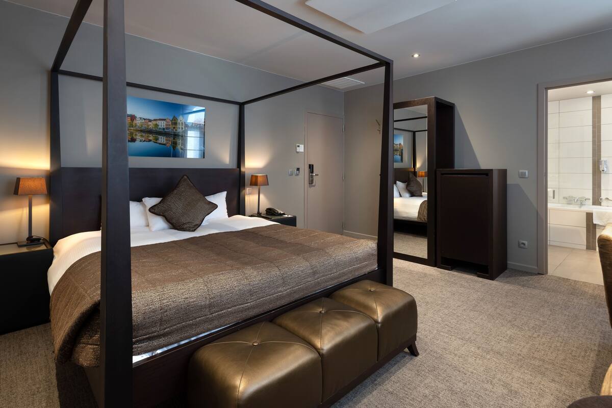Habitación de hotel moderna con cama con dosel, un espejo grande y vistas de la ciudad a través del ventanal.