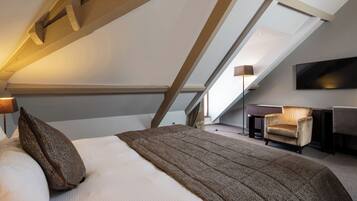 Ein Schlafzimmer mit schrägem Dach, einem Bett, einem Sessel, einem Fernseher und einem Schreibtisch.