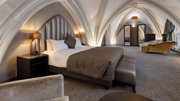 Una habitación de hotel moderna con una cama grande, un área de descanso y vistas a la ciudad.